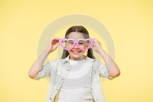 Happy child wear heart shaped glasses on yellow background. Little girl smile in fashion accessory. Summer fashion look
