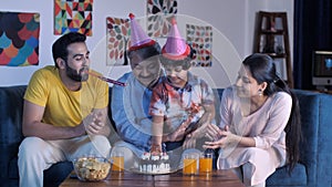 A happy child wearing a colorful hat blowing candles while celebrating his birthday