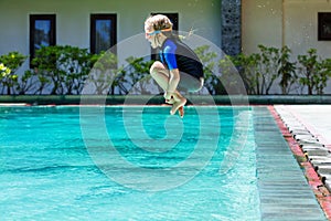 Happy child in wetsuit has fun jumping into swimming pool