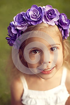 Happy child in wreath of flowers outdoors in summer park