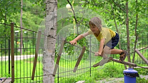 Happy child in a yellow teashirt, school boy enjoys activity in a climbing adventure park