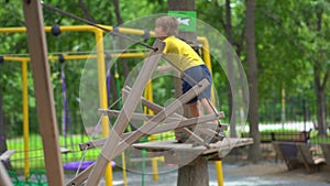 Happy child in a yellow teashirt, school boy enjoys activity in a climbing adventure park