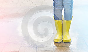 Happy child in yellow wellington boot jumps in a puddle of water after rain. Cheerful baby on a summer sunny day