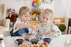 Happy childen, siblings, coloring eggs for Easter at home, sunny room