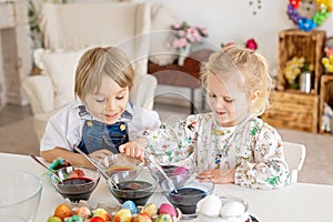 Happy childen, siblings, coloring eggs for Easter at home, sunny room