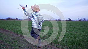 Happy childhood, boy with airplane in hands runs along green field in slow motion