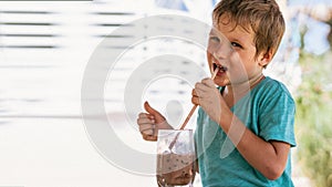 Happy childhood. Boy drinking chocolate tea with ice in hot summer day time. Cute lover of sweets and tasty things