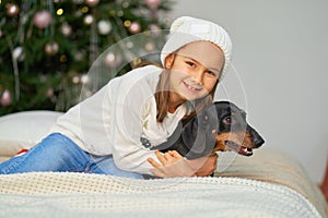 Happy childhood, Christmas magic fairy tale. A little girl is laughing with her friend, a dachshund dog, near the Christmas tree