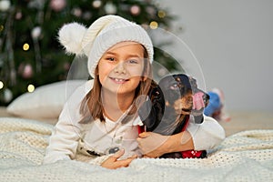 Happy childhood, Christmas magic fairy tale. A little girl is laughing with her friend, a dachshund dog, near the Christmas tree