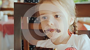 Happy childhood, cool girl eating chocolate cake in a cafe on the street, the whole face is covered with chocolate