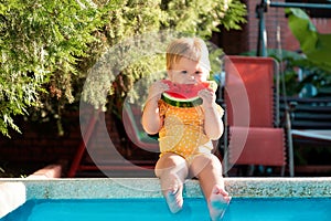 Happy childhood. Cute Caucasian little girl in yellow swimwear eating a slice of fresh watermelon. Child sitting by a