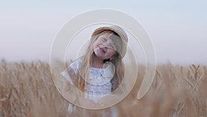 Happy childhood, little beautiful fair haired child girl smiles and turns her head standing in golden grain wheat spikes