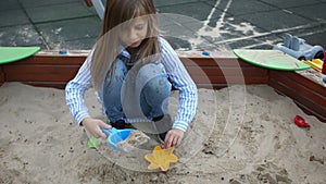 Happy childhood. Weekdays at the playground. Girl preschool girl with long hair plays in the sandbox with a shovel and