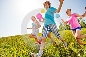 Happy children with balloons run in green field