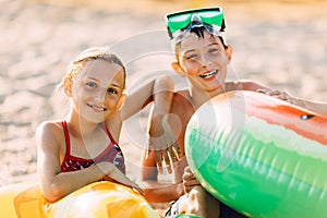 Happy children boy and girl with inflatable circle, play and have fun sitting on the sand on the beach enjoy summer vacation