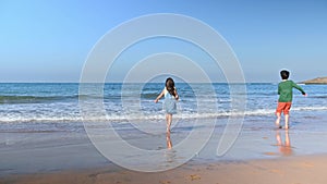 Happy children boy and girl playing barefoot on the tropical beach, playing waves on the sandy beach