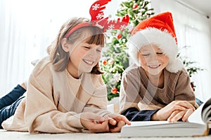 Happy children, a boy and a girl, read a book on Christmas or New Year's Eve against the background of a Christmas