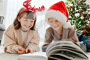 Happy children, a boy and a girl, read a book on Christmas or New Year's Eve against the background of a Christmas