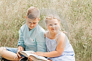 Happy children, boy and girl reading the book under in summer on nature
