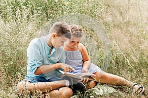 Happy children, boy and girl reading the book under in summer on nature