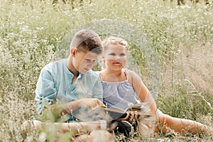 Happy children, boy and girl reading the book under in summer on nature