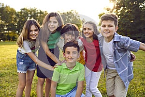 Happy children boys and girls from elementary school stand around friend on lawn summer park