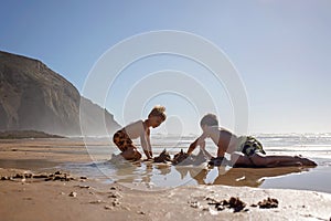 Happy children, boys, playing on the beach on sunset, kid cover in sand, smiling, laughing