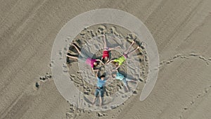 Happy children in bright clothes lie on the sand in the shape of a star