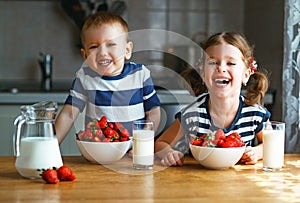 Happy children brother and sister eating strawberries with milk