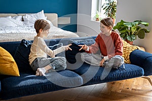 Happy children brother and sister sit on sofa play rock-paper-scissors game together at home