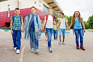 Happy children carry rucksacks, walk near school