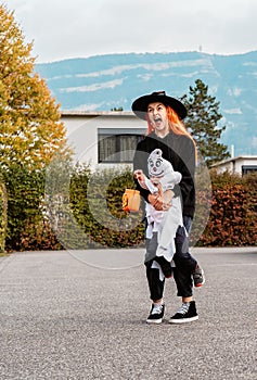 Happy children in costumes trick-or-treating on street outdoors with pumpkin bag collecting candies celebrating Halloween