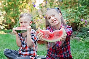Happy children eating watermelon in the garden. Kids eat fruit outdoors. Little girl and boy playing in the garden biting a slice