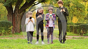 Happy children friend girls group walk together in summer park and playing internet game with mobile smartphone. kids