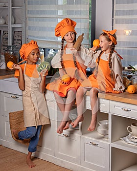 Happy children friends eating fresh orange and playing with fresh mandarin fruits in kitchen at home.