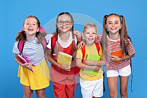 Happy children, girls and boys, standing with backpacks behind and exercise books, smiling at camera