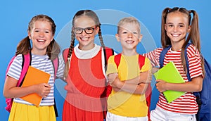 Happy children, girls and boys, standing with backpacks behind and exercise books, smiling at camera