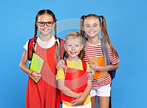 Happy children, girls and boys, standing with backpacks behind and exercise books, smiling at camera