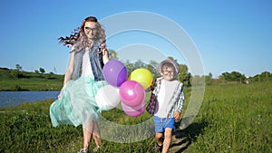 Happy children in glasses with colored balloons in hands have fun on green lawn near lough