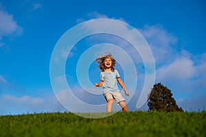 Happy children on green grass. Smiling kid having fun in spring park on blue sky. Healthy lifestyle concept.