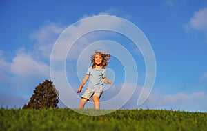 Happy children on green grass. Smiling kid having fun in spring park on blue sky. Healthy lifestyle concept.