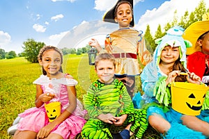 Happy children in Halloween costumes sit on grass