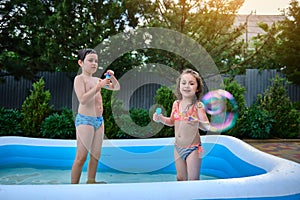 Happy children have fun, blowing soap bubbles in the inflatable pool at house backyard garden. Summer childhood days.