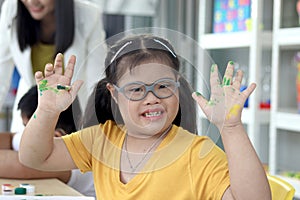 Happy children have fun with friends during study at school, smiling girl with down syndrome showing his painted hands at art