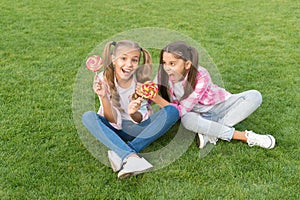 Happy children hold candy sit grass. Sugar and calories. Joyful cheerful friends eating sweets outdoors. Candy shop