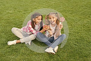 Happy children hold candy sit grass. Sugar and calories. Joyful cheerful friends eating sweets outdoors. Candy shop