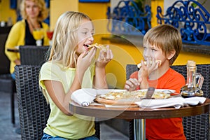 Happy children indoors eating pizza smiling