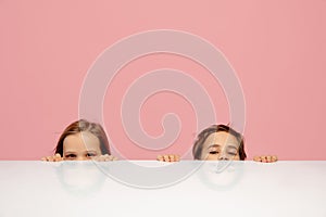 Happy children isolated on coral pink studio background. Look happy, cheerful, sincere. Copyspace. Childhood, education