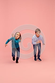 Happy children isolated on coral pink studio background. Look happy, cheerful, sincere. Copyspace. Childhood, education