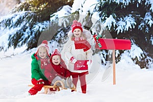 Children with letter to Santa at Christmas mail box in snow